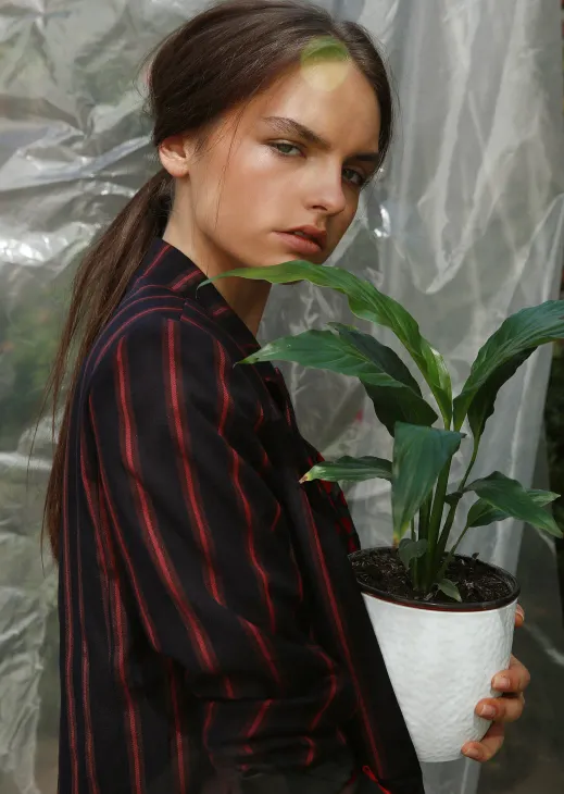 Modelo con blazer a rayas sosteniendo una planta en un macetero blanco