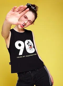Modelo con polera negra estampada frente a un fondo amarillo, tapando la cámara con la mano