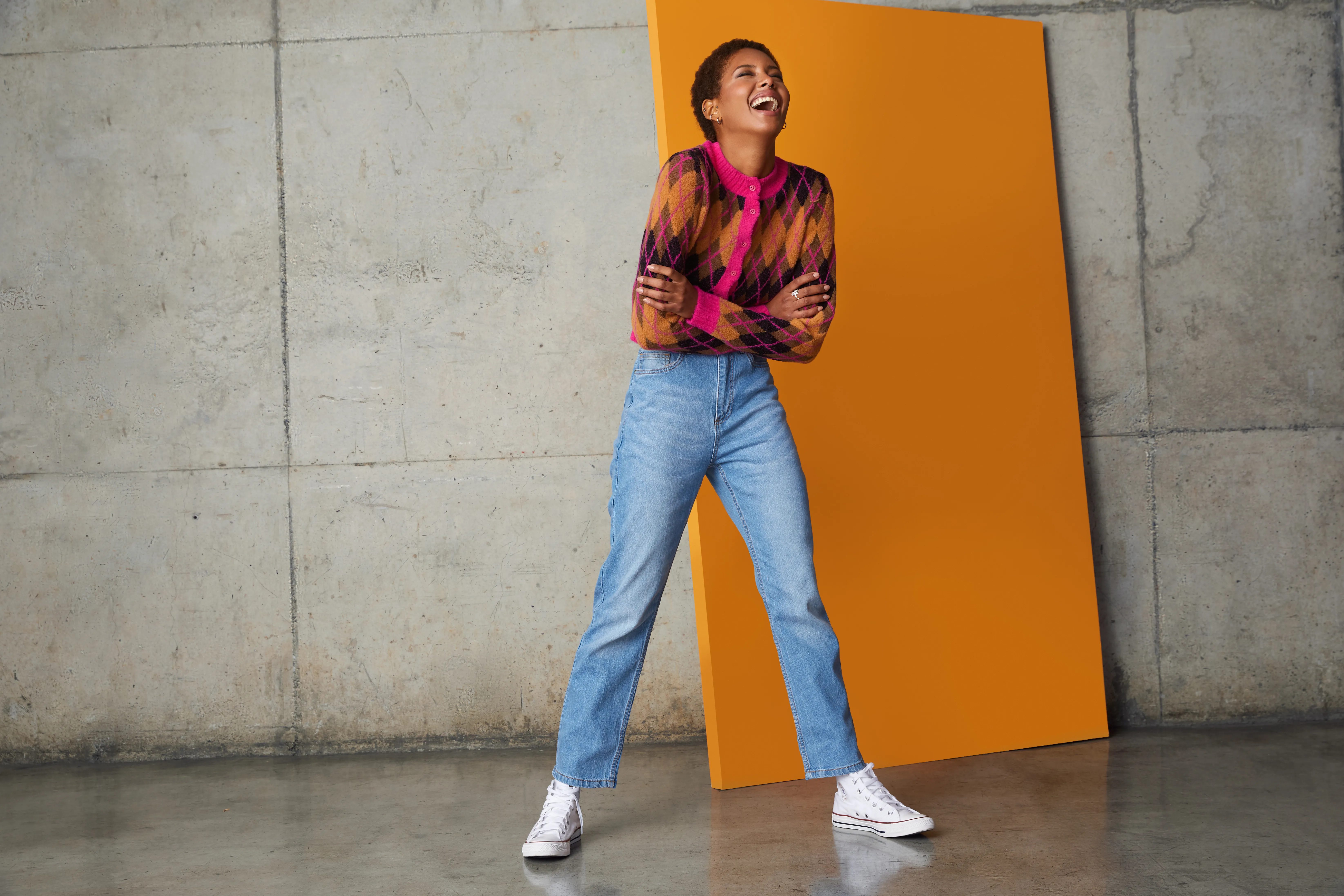 Modelo con camisa estampada y jeans frente a un panel naranjo