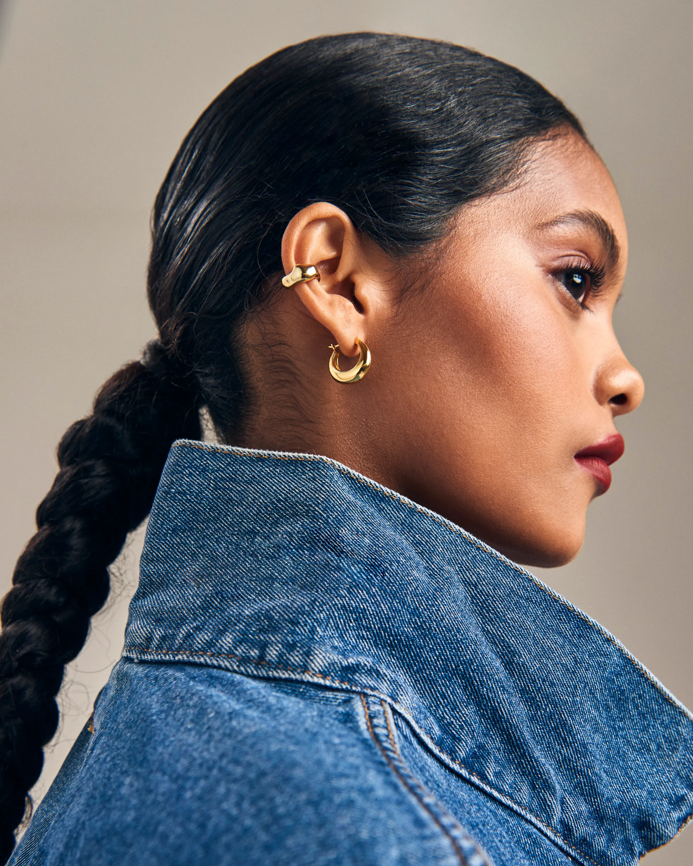 Retrato de perfil de modelo con trenza, aros dorados y chaqueta de mezclilla