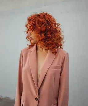 Modelo de pelo colorín rizado con blazer rosado