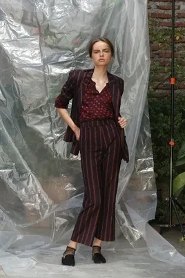 Modelo con traje a rayas y blusa estampada frente a un plástico translúcido